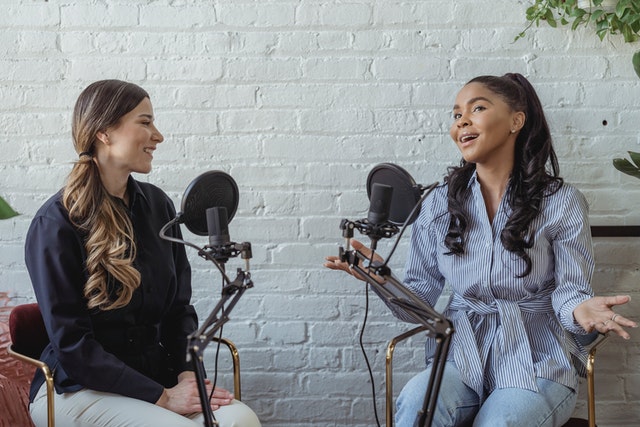 Two women talk to each other while sitting in front of microphones